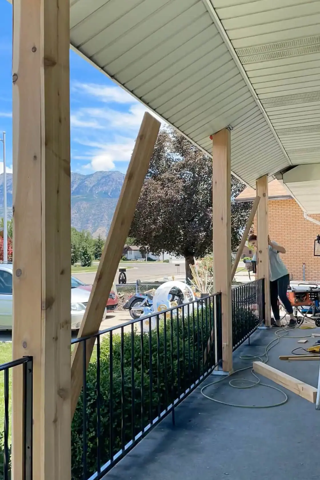 Wide view of multiple porch posts being wrapped with natural wood boards during a DIY project to update a traditional front porch with modern farmhouse style.